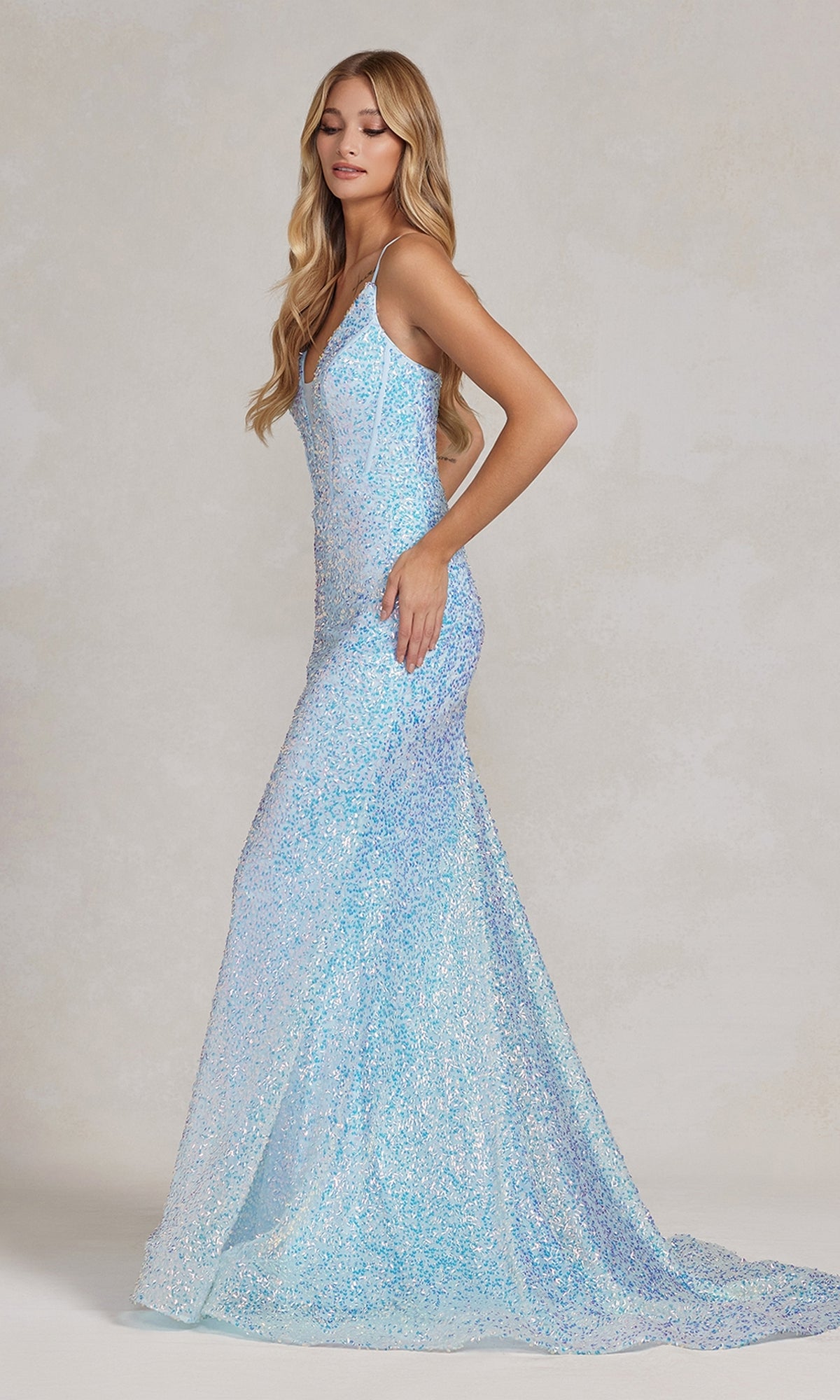 A woman wearing the Corset-Back Deep V-Neck Long Sequin Prom Dress, a fitted, floor-length light blue gown with thin straps, stands against a neutral background.